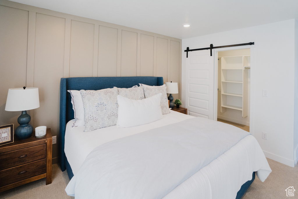 Bedroom featuring a decorative wall, light colored carpet, a walk in closet, and a barn door