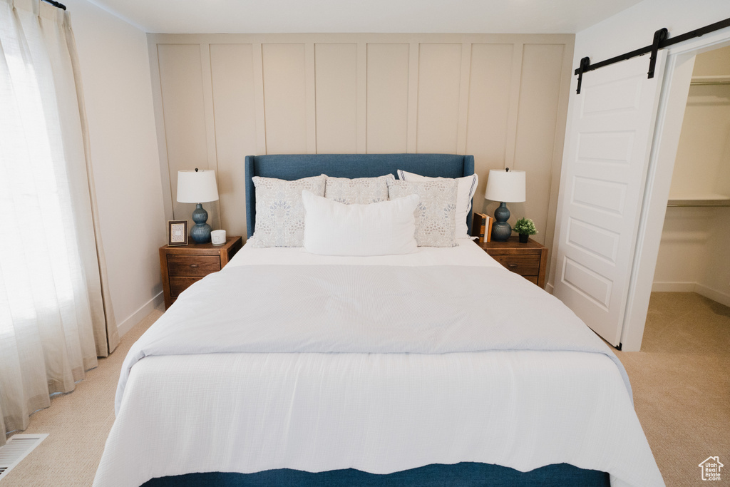 Bedroom with visible vents, a barn door, a decorative wall, a walk in closet, and light colored carpet