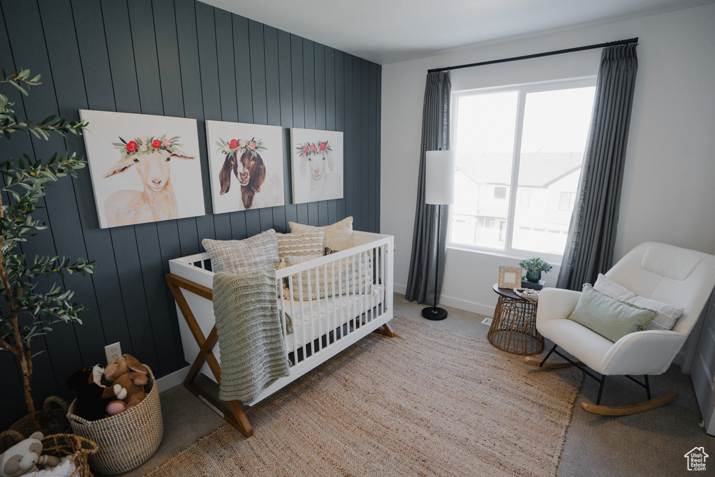 Bedroom with wood walls, baseboards, carpet flooring, and a crib