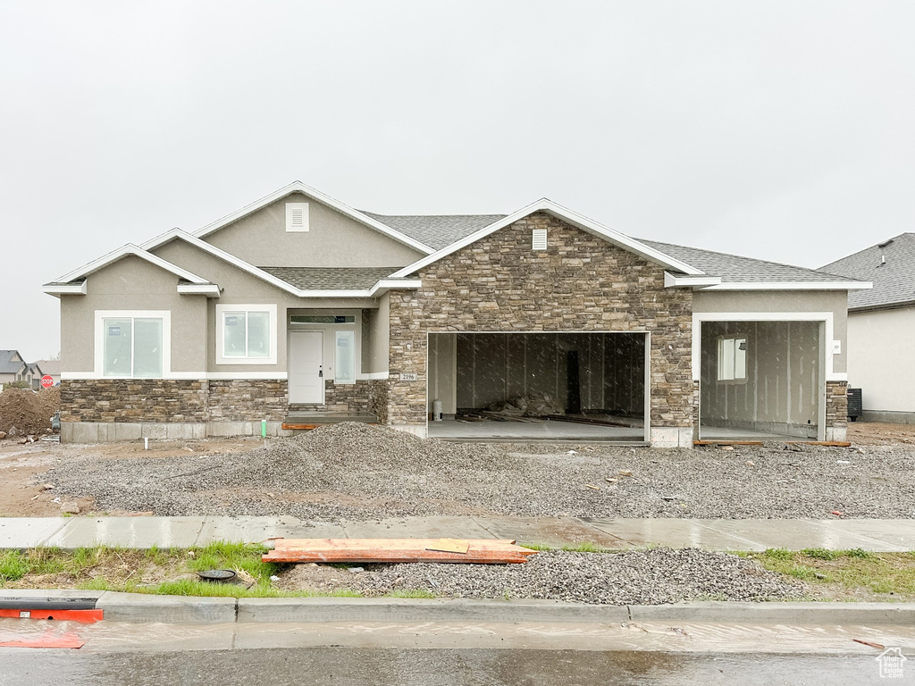 Craftsman-style house with stone siding, roof with shingles, gravel driveway, stucco siding, and a garage