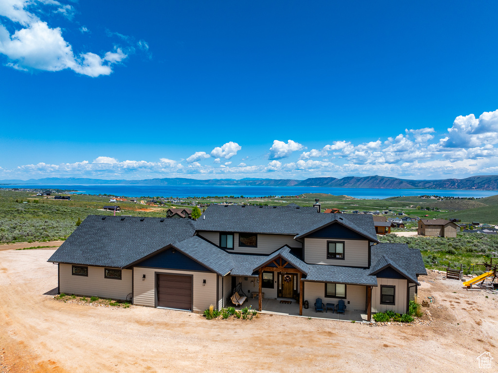 View of front facade featuring roof with shingles, a garage, driveway, a porch, and a water and mountain view