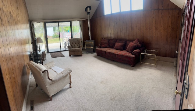 Living area featuring carpet, lofted ceiling, a wood stove, and wood walls