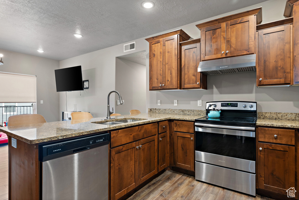 Kitchen with a peninsula, under cabinet range hood, visible vents, stainless steel appliances, and a sink