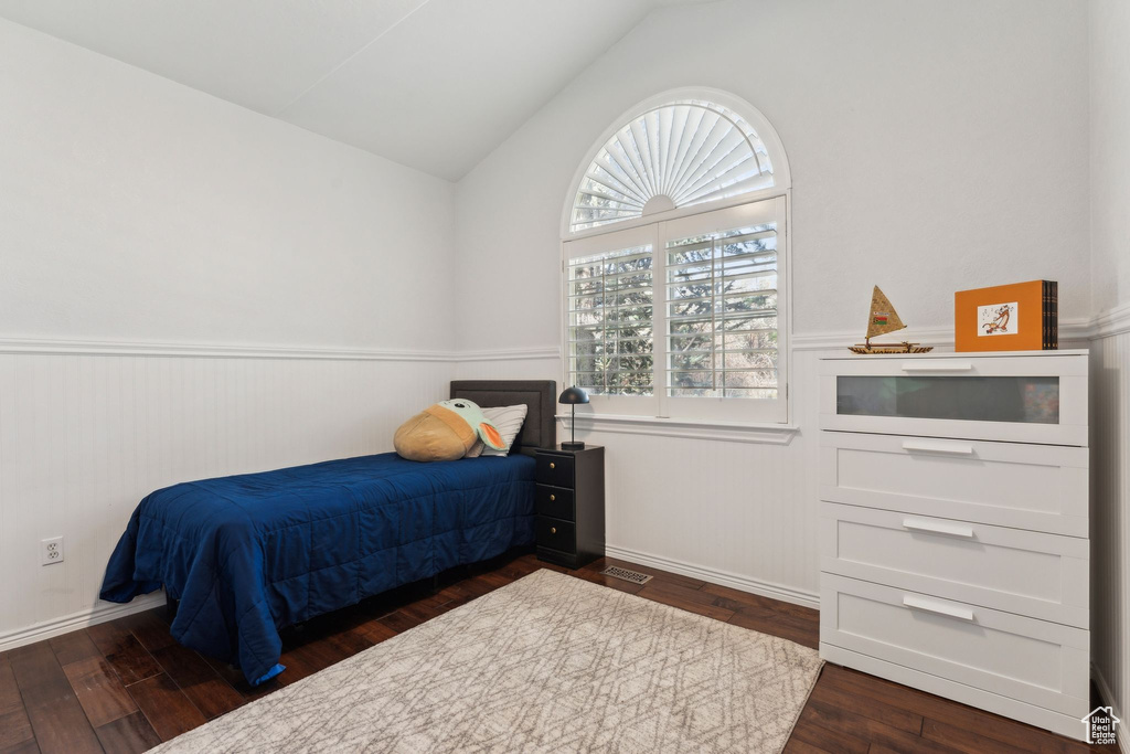 Bedroom with dark wood-style flooring, vaulted ceiling, and a wainscoted wall
