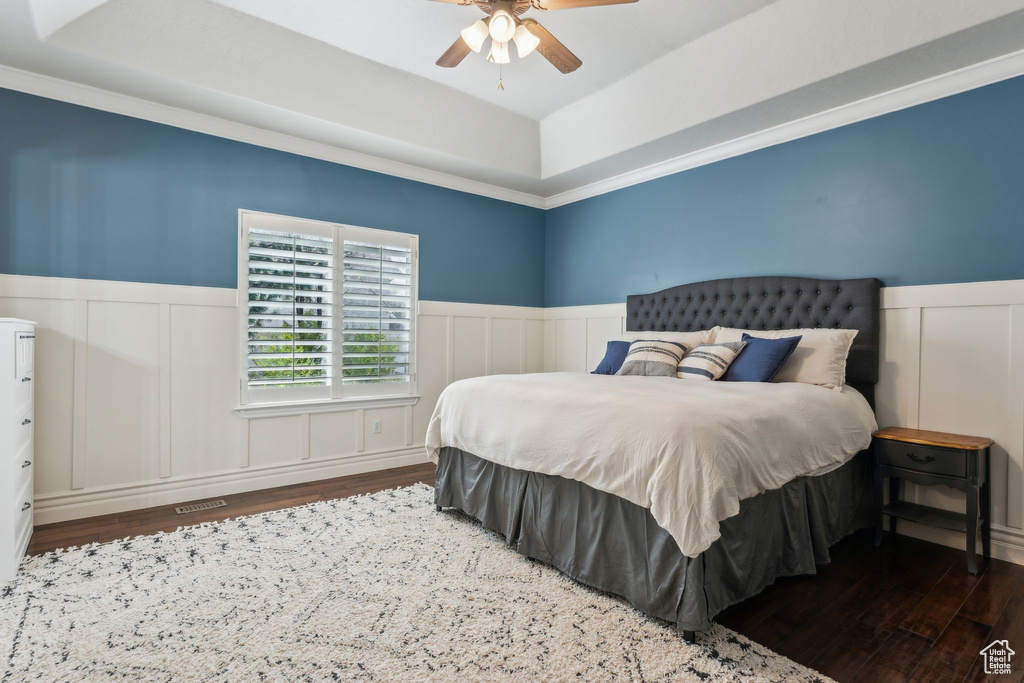 Bedroom with a decorative wall, a tray ceiling, and wood finished floors