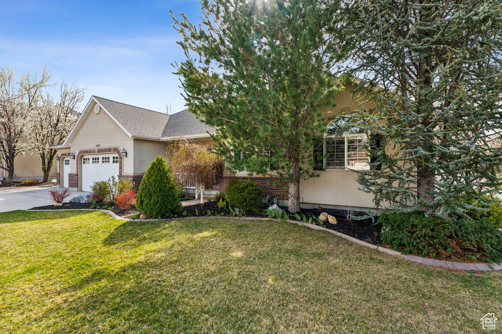 View of front facade featuring a front yard, a garage, concrete driveway, brick siding, and stucco siding