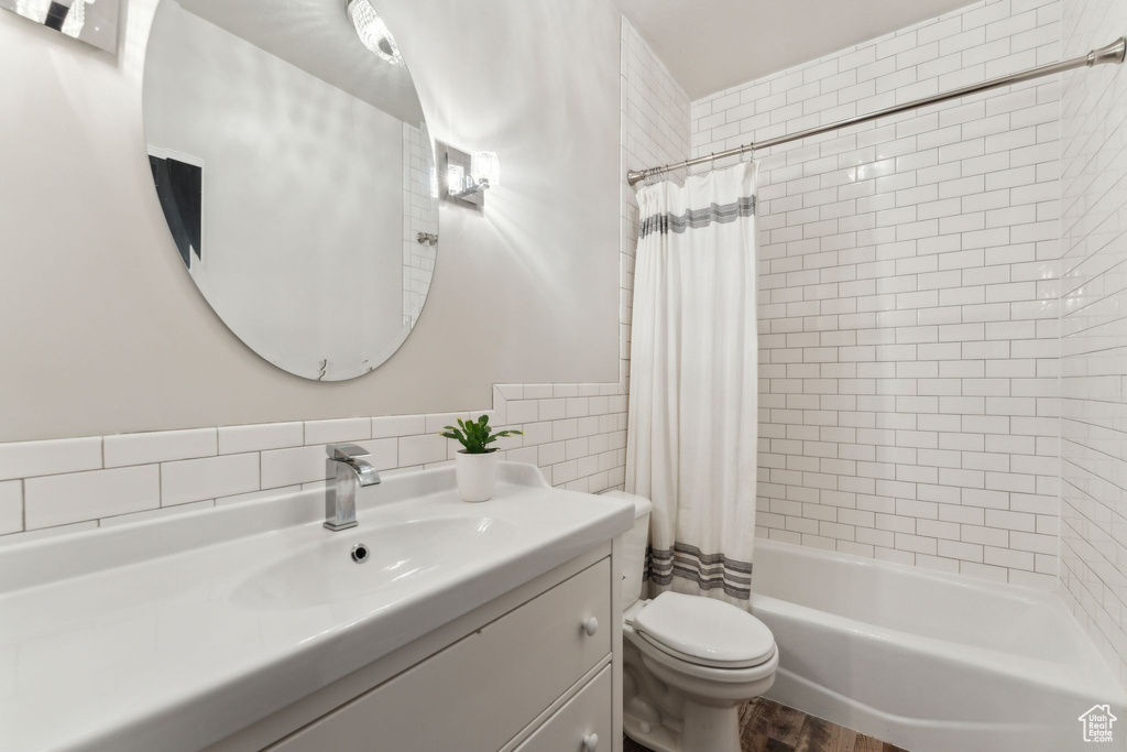 Bathroom featuring shower / bath combination with curtain, toilet, tile walls, vanity, and wood finished floors
