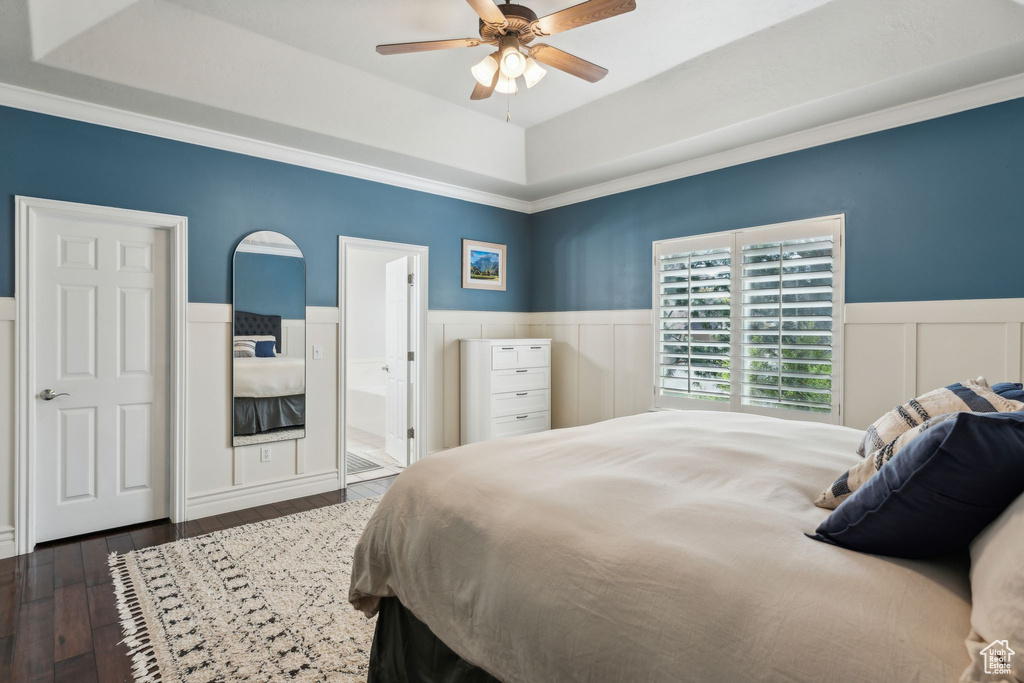 Bedroom featuring ensuite bathroom, a tray ceiling, a ceiling fan, wood finished floors, and wainscoting
