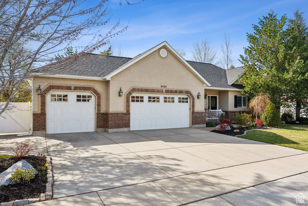 View of front of home with concrete driveway, stucco siding, brick siding, a garage, and a shingled roof