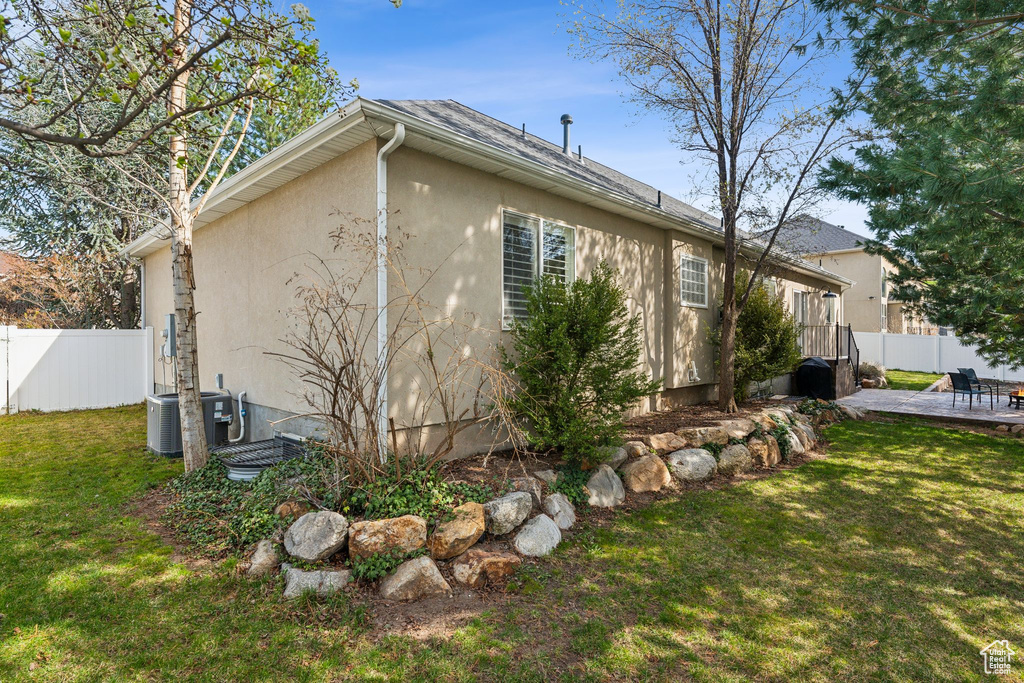View of property exterior with stucco siding, cooling unit, a patio area, a yard, and fence