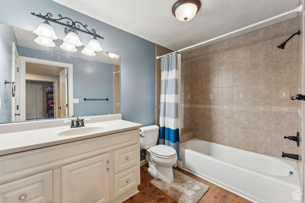 Full bath with toilet, vanity, wood finished floors, and shower / bath combination with curtain