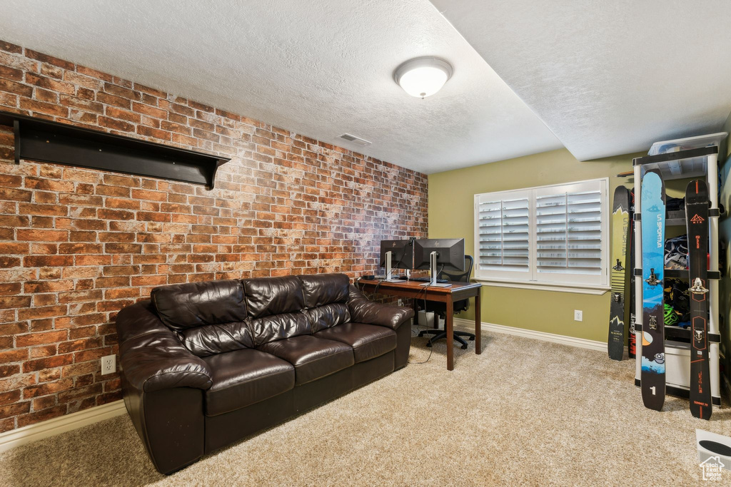 Carpeted office space featuring visible vents, baseboards, brick wall, and a textured ceiling