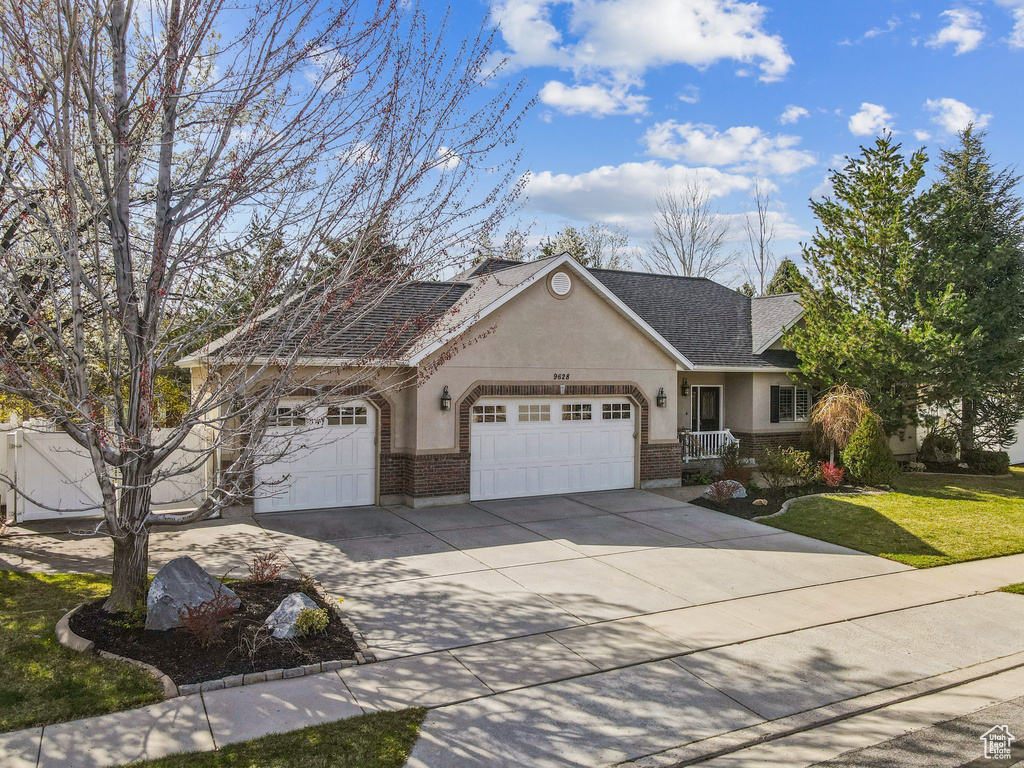 View of front of property with stucco siding, a front lawn, brick siding, a garage, and driveway