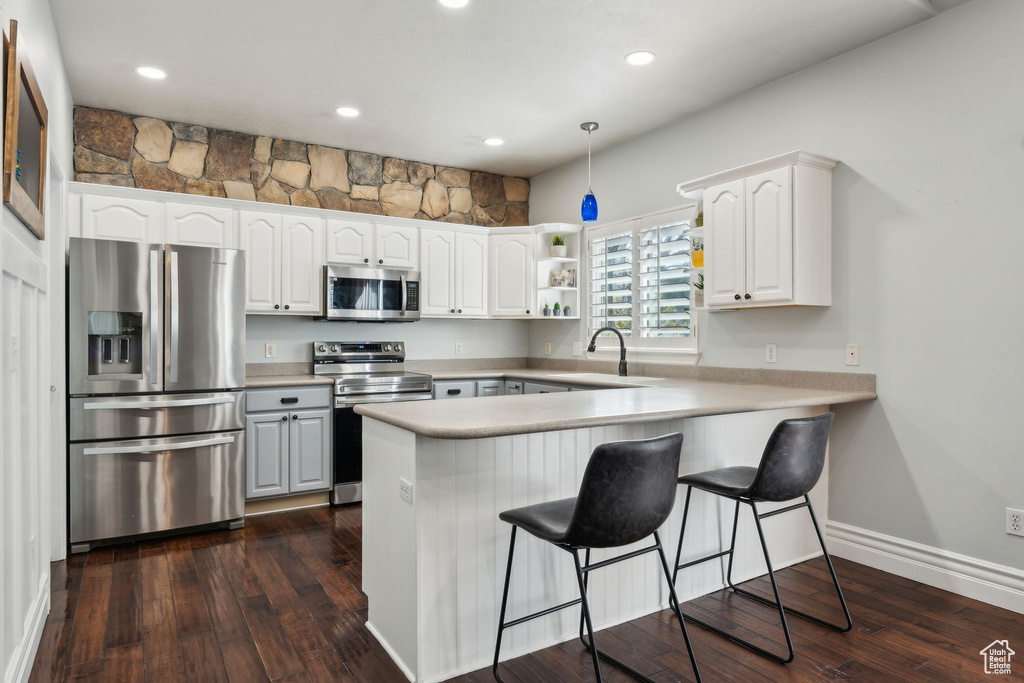 Kitchen with white cabinets, appliances with stainless steel finishes, a breakfast bar, a peninsula, and dark wood-style floors