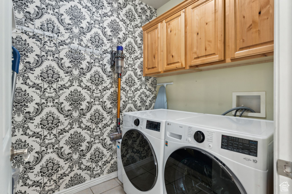 Clothes washing area with light tile patterned flooring, washing machine and clothes dryer, and cabinet space