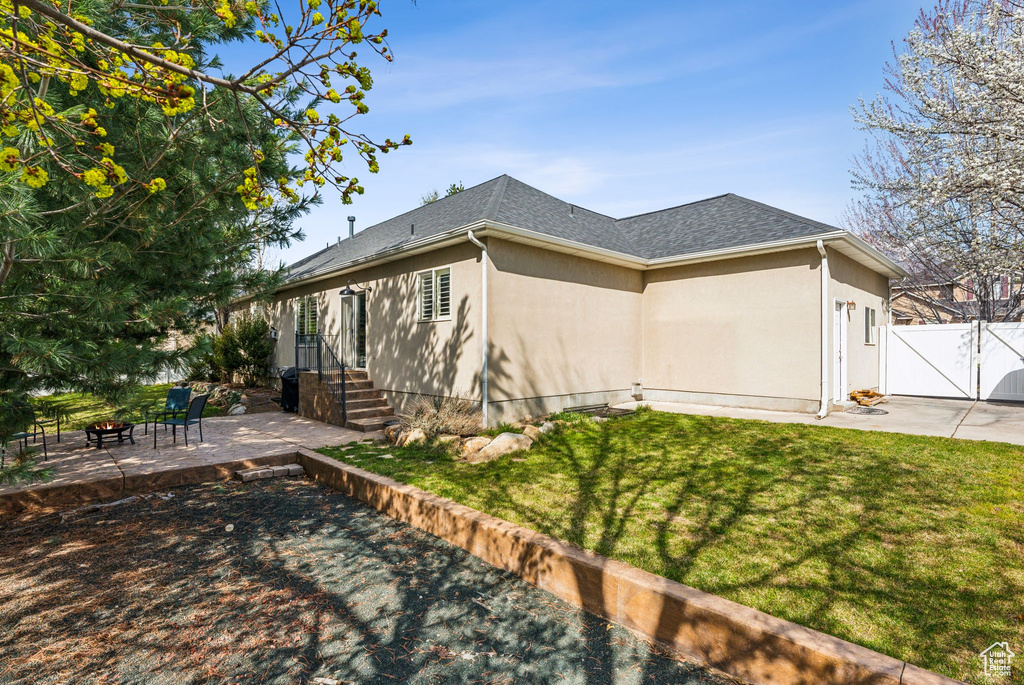 View of side of home with a lawn, a patio, roof with shingles, fence, and a gate