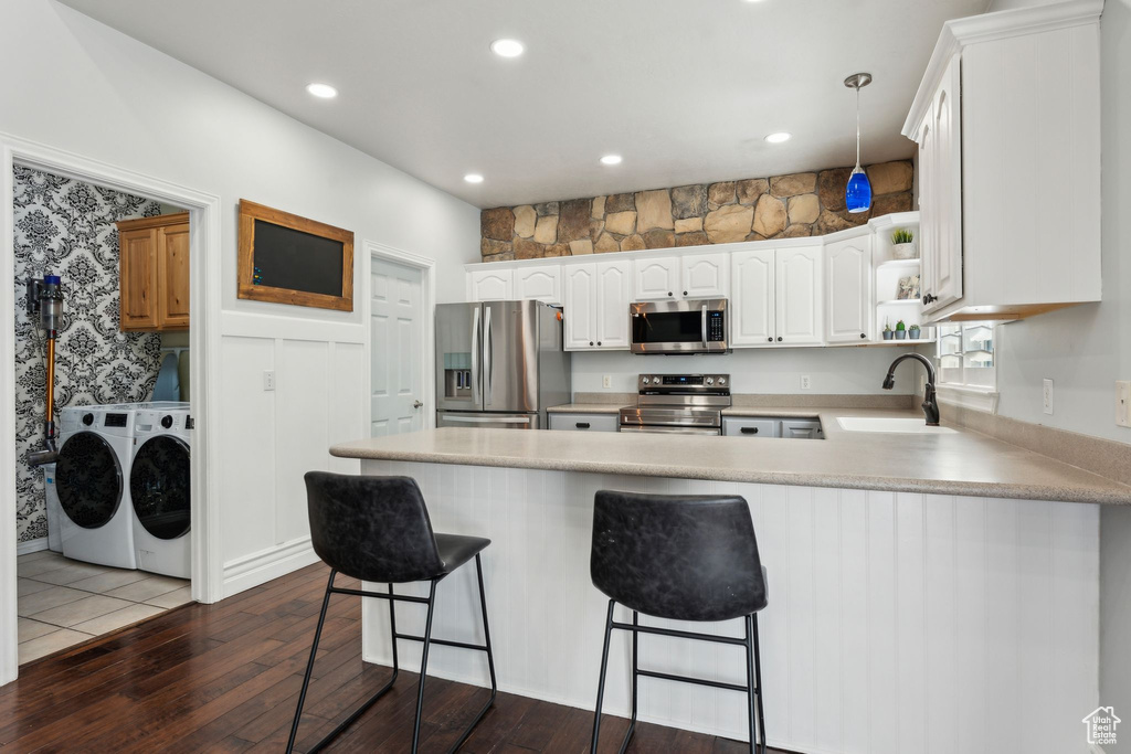 Kitchen with dark wood-style flooring, a peninsula, washing machine and clothes dryer, stainless steel appliances, and a sink