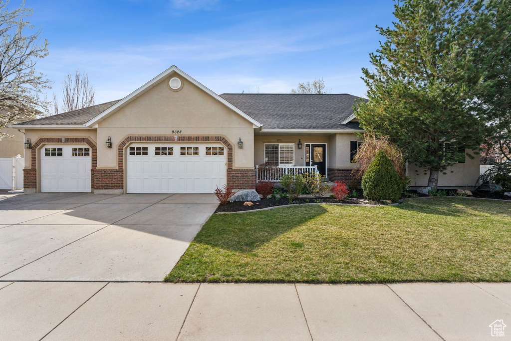 Single story home with stucco siding, a front yard, brick siding, an attached garage, and driveway