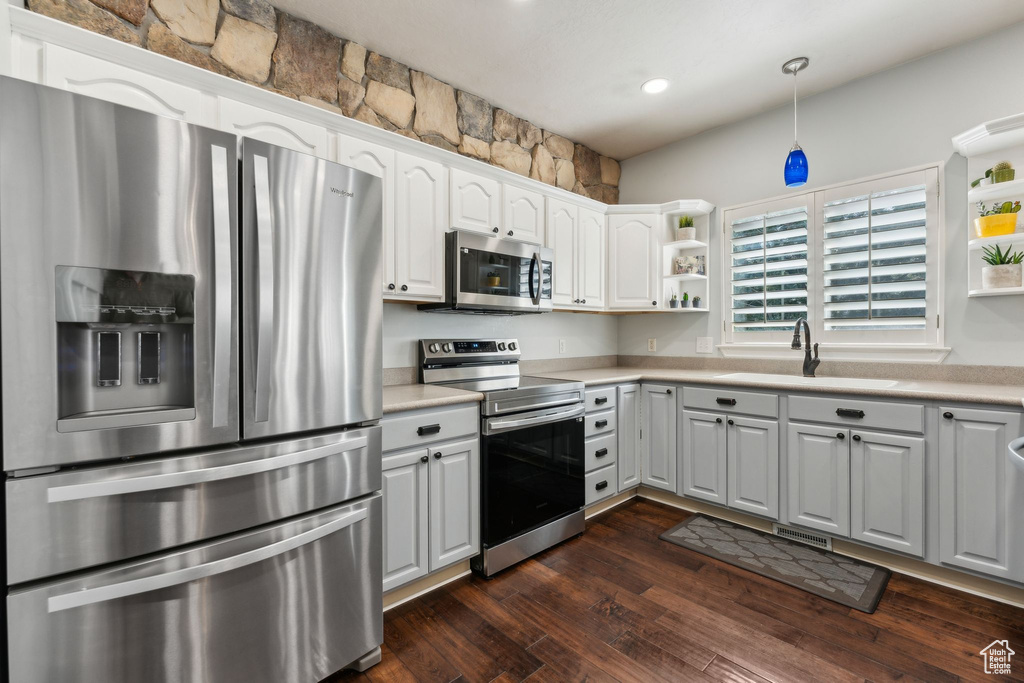 Kitchen featuring stainless steel appliances, light countertops, a sink, and open shelves