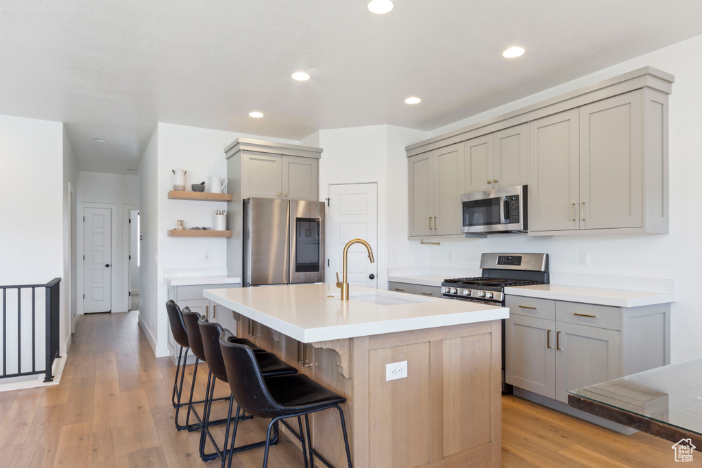 Kitchen featuring a kitchen bar, open shelves, a sink, stainless steel appliances, and gray cabinetry