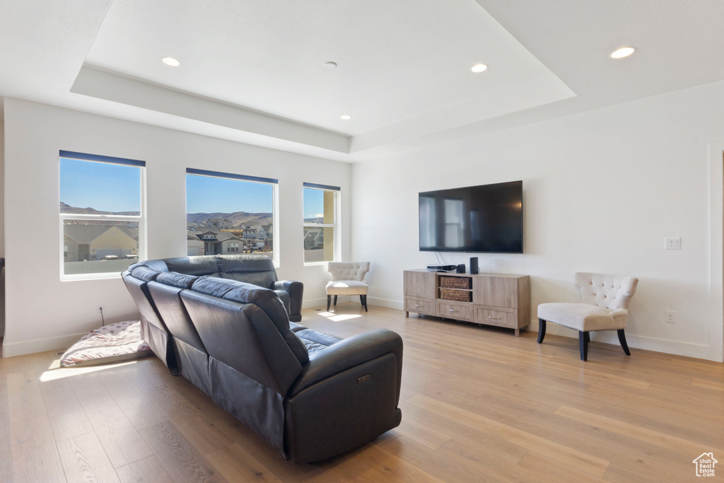 Living room featuring recessed lighting, light wood-style flooring, a tray ceiling, and baseboards