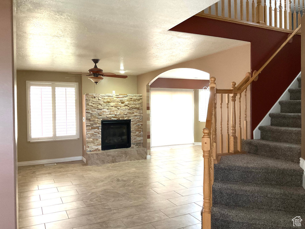 Living area featuring arched walkways, a ceiling fan, stairs, a fireplace, and baseboards