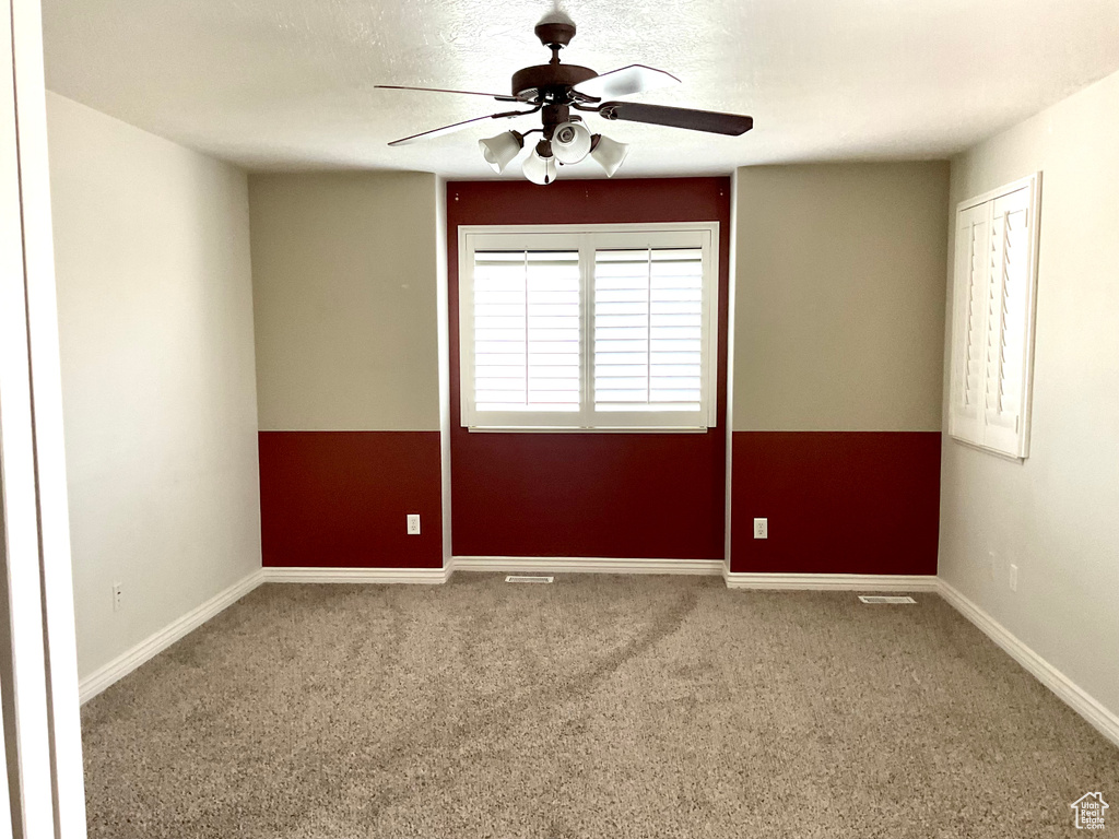 Carpeted empty room featuring a ceiling fan and baseboards
