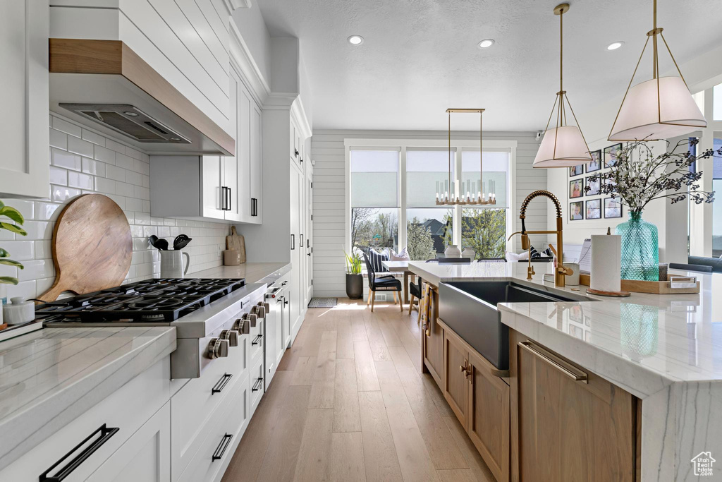 Kitchen with a sink, premium range hood, stainless steel gas stovetop, a large island with sink, and backsplash