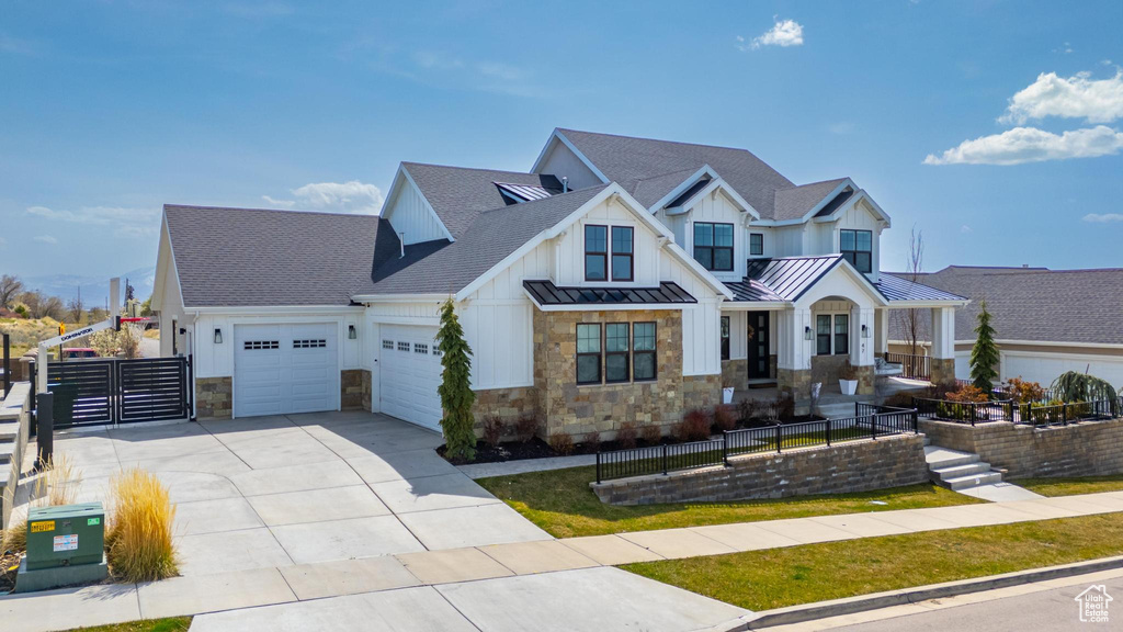 View of front facade featuring an attached garage, stone siding, fence, concrete driveway, and a standing seam roof