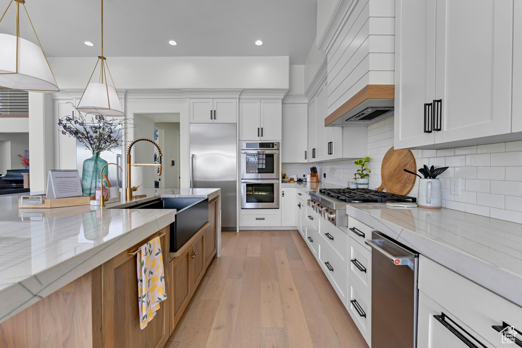 Kitchen featuring tasteful backsplash, a sink, stainless steel appliances, light wood-style flooring, and light stone counters