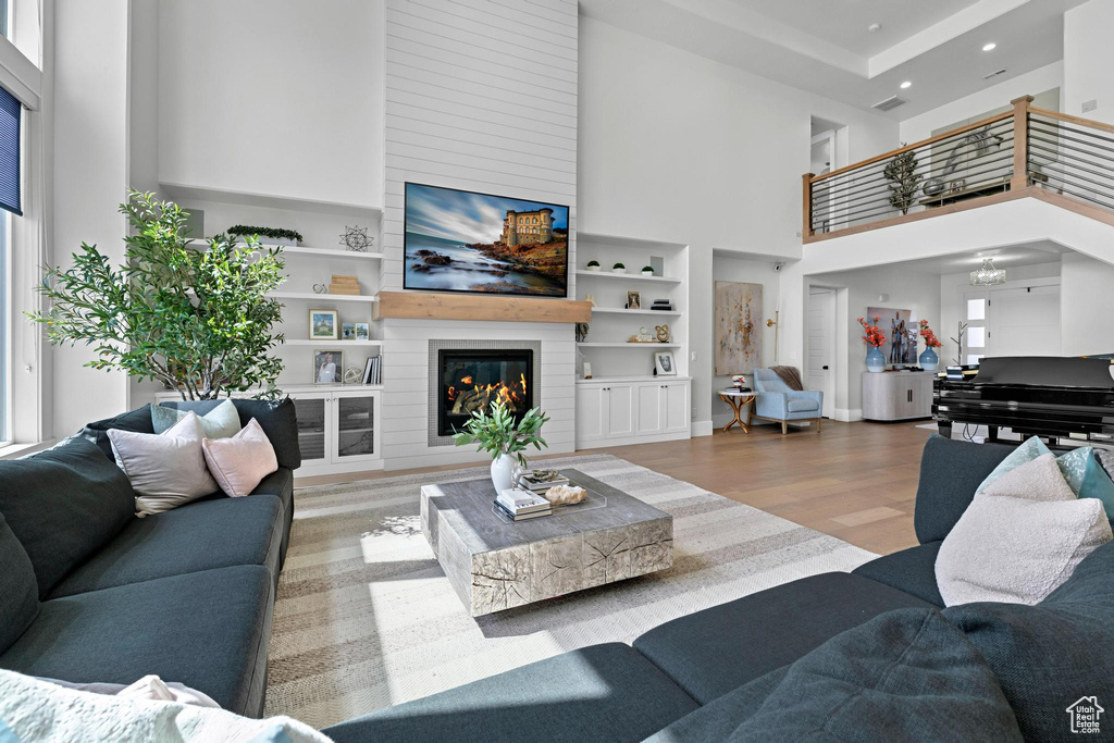 Living room with a towering ceiling, built in features, recessed lighting, a fireplace, and wood finished floors