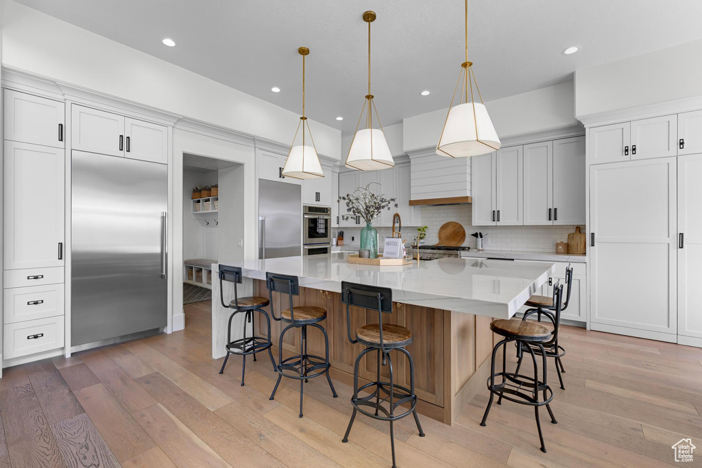 Kitchen with decorative backsplash, recessed lighting, appliances with stainless steel finishes, light wood finished floors, and a spacious island