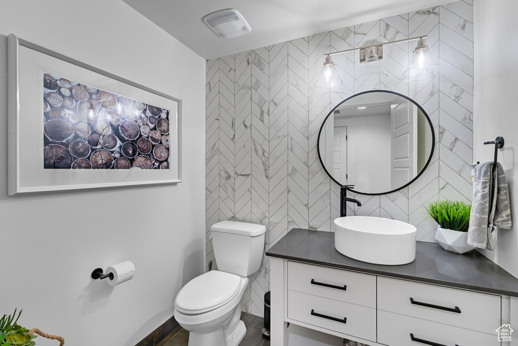 Bathroom with vanity, visible vents, toilet, tile walls, and backsplash