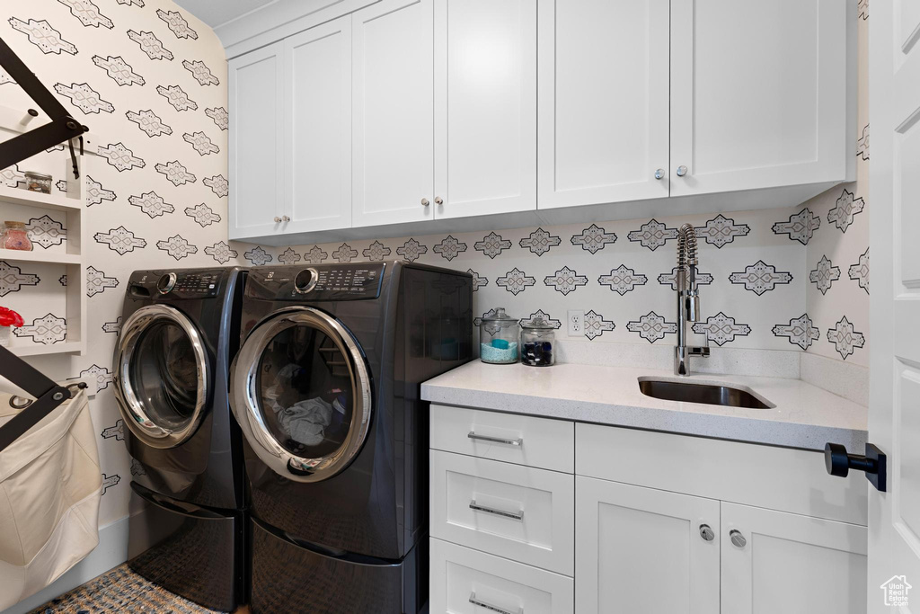 Washroom with wallpapered walls, washer and dryer, a sink, and cabinet space