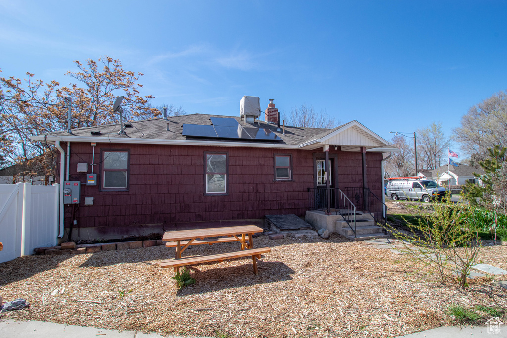 Back of property with a chimney, fence, solar panels, and roof with shingles