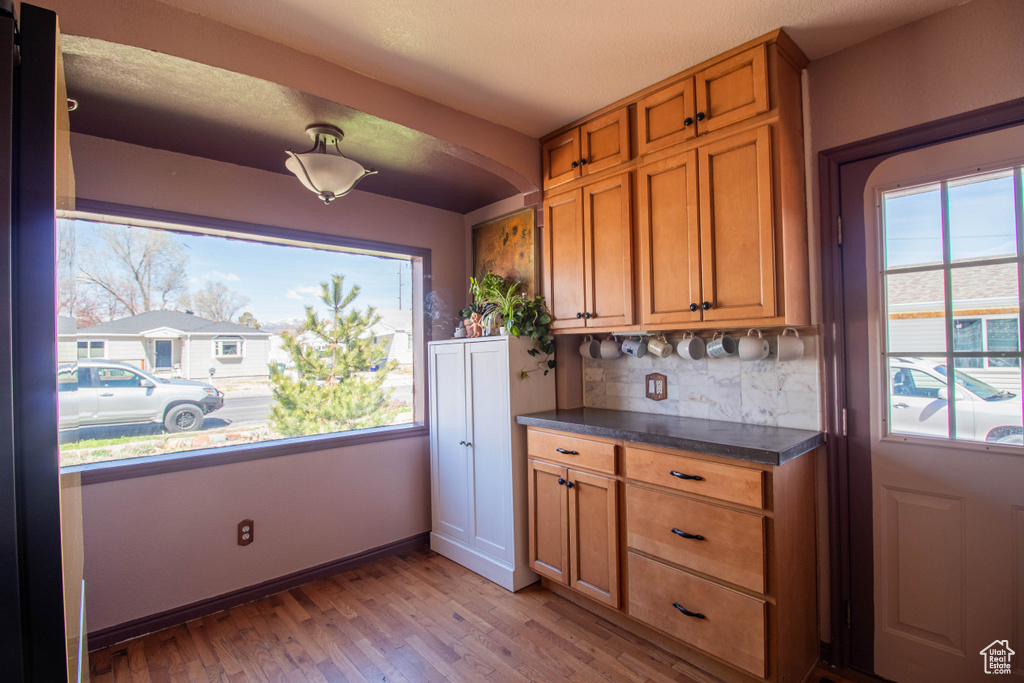 Kitchen with brown cabinetry, light wood-type flooring, dark countertops, and a wealth of natural light
