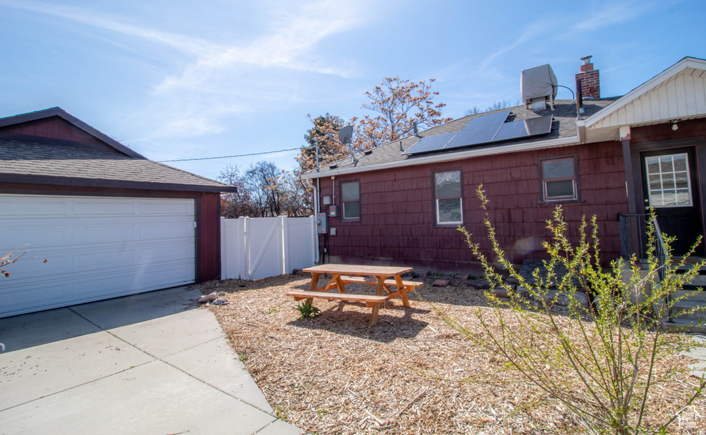 View of side of property with fence, a shingled roof, a garage, and roof mounted solar panels