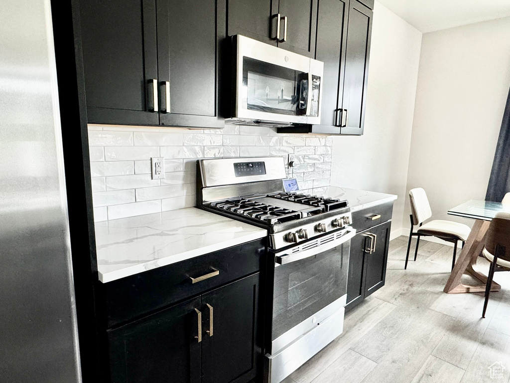 Kitchen featuring appliances with stainless steel finishes, dark cabinets, light stone counters, and decorative backsplash
