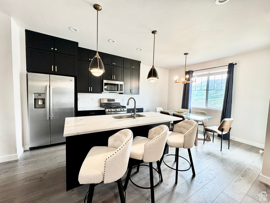 Kitchen with appliances with stainless steel finishes, dark cabinetry, a sink, light wood-style flooring, and recessed lighting
