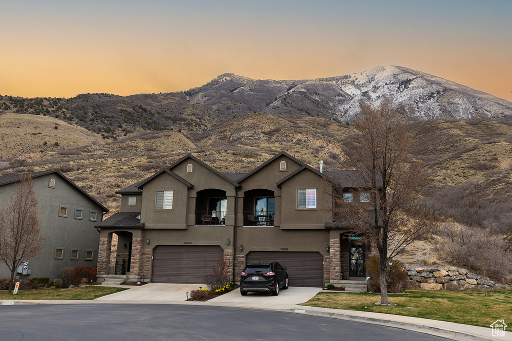 View of front of house with a mountain view, stone siding, a garage, and stucco siding