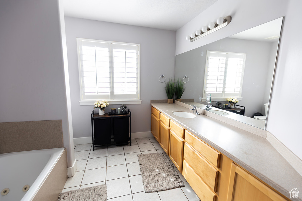 Bathroom with baseboards, toilet, a jetted tub, vanity, and tile patterned flooring