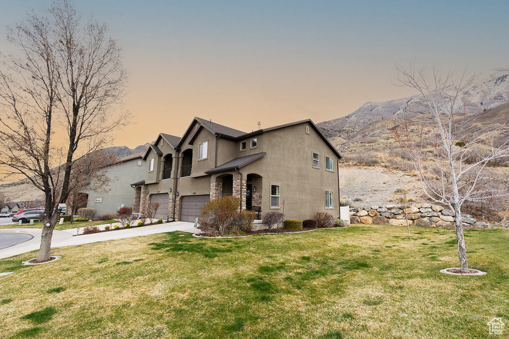 View of front of property with stucco siding, a mountain view, driveway, an attached garage, and a yard