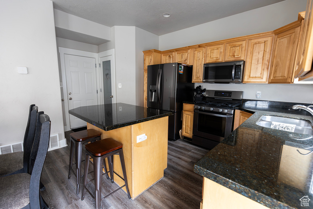 Kitchen featuring dark wood-style floors, a center island, stainless steel gas range oven, black refrigerator with ice dispenser, and a sink