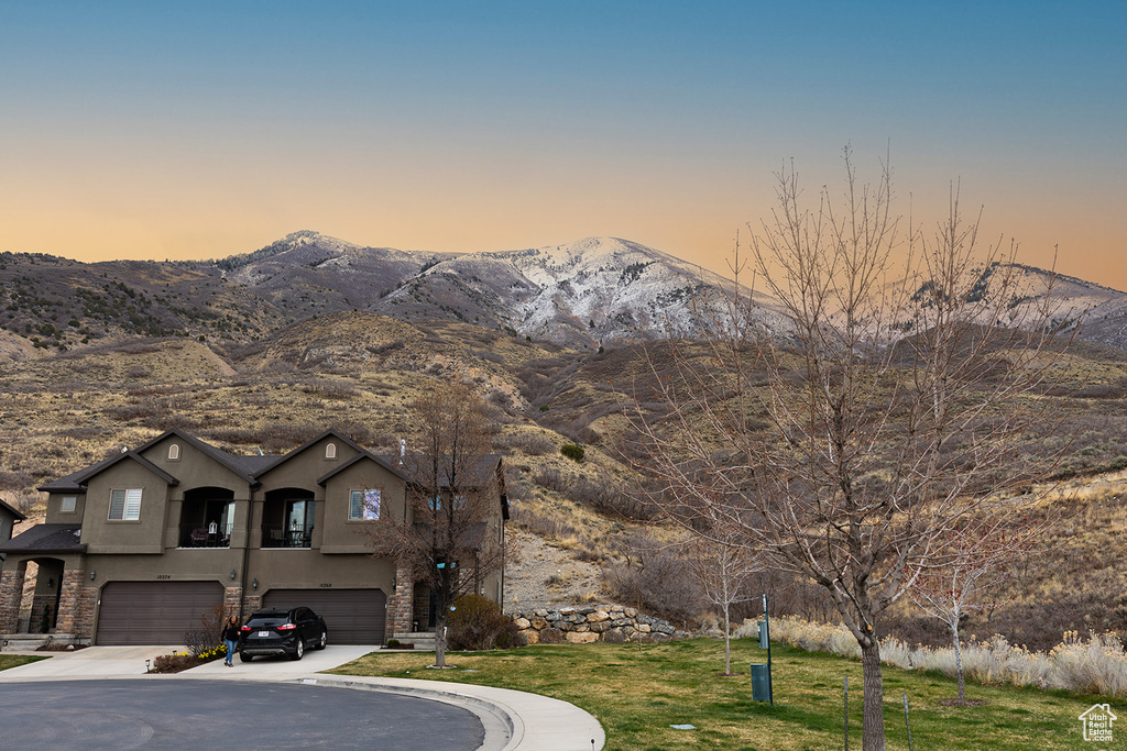 View of front of home with stucco siding, a lawn, an attached garage, a mountain view, and concrete driveway