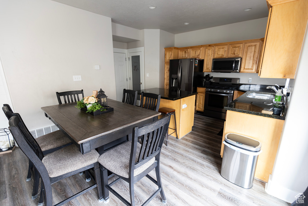 Kitchen with a kitchen island, appliances with stainless steel finishes, a sink, dark countertops, and light wood finished floors