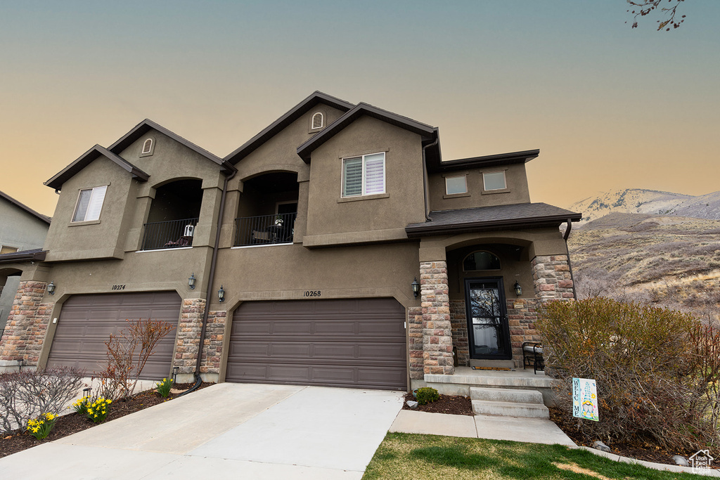 View of front of home with a garage, stucco siding, stone siding, a mountain view, and concrete driveway