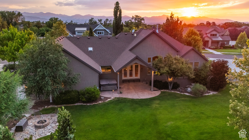 Back of property at dusk featuring a patio, a lawn, stucco siding, and an outdoor fire pit