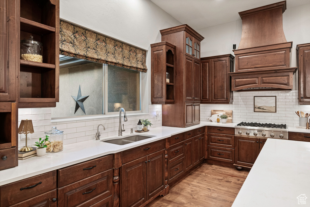 Kitchen featuring open shelves, stainless steel gas cooktop, light countertops, light wood-style floors, and tasteful backsplash