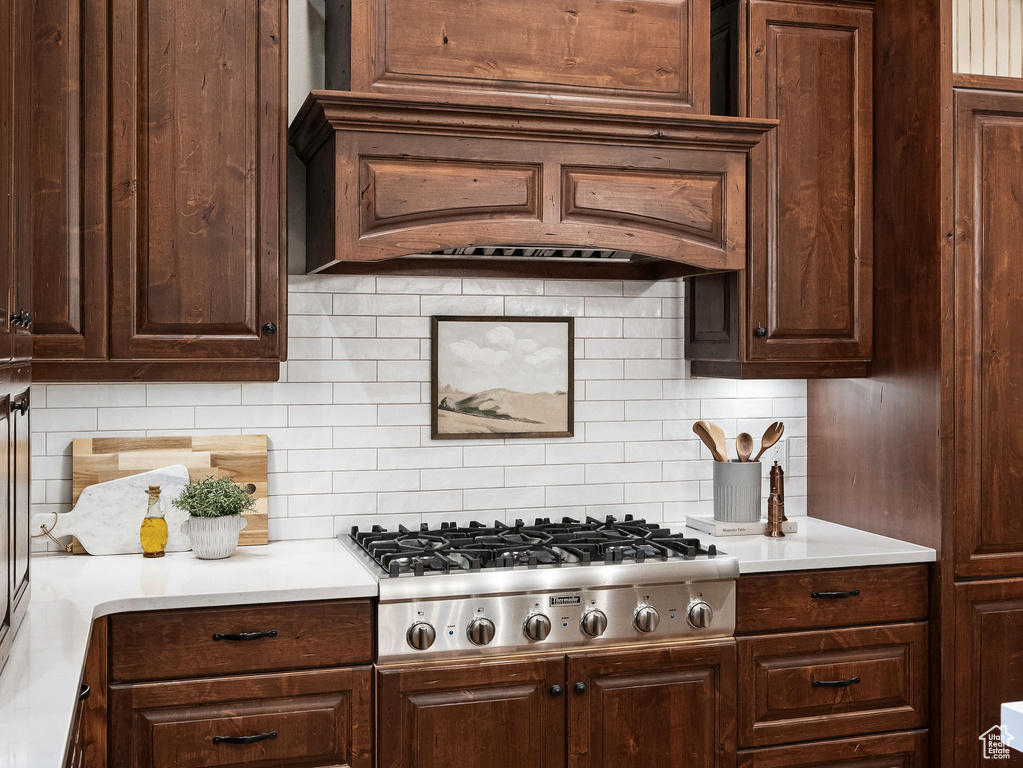 Kitchen with stainless steel gas stovetop, backsplash, light countertops, wood finished floors, and dark brown cabinetry