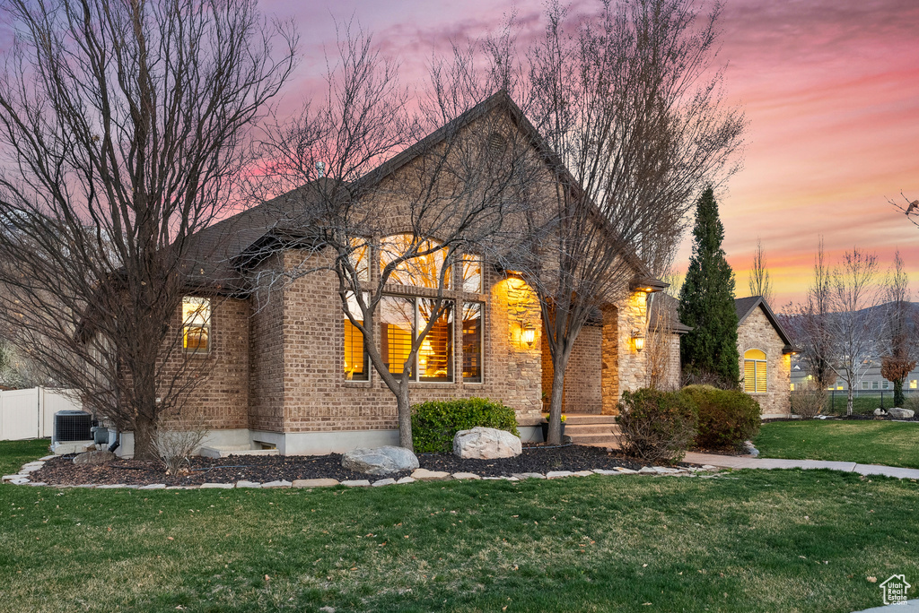 French country inspired facade featuring fence, cooling unit, brick siding, and a lawn